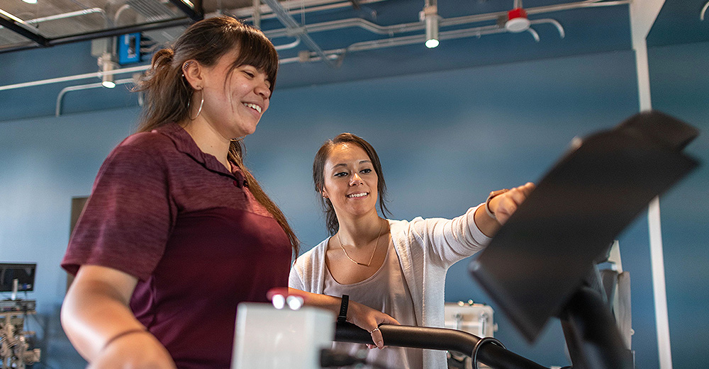 One female student is showing another female student how to use the treadmill 