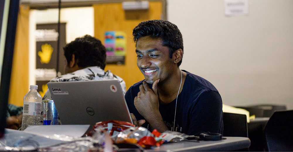 Smiling male student sitting in a classroom while looking at his laptop computer