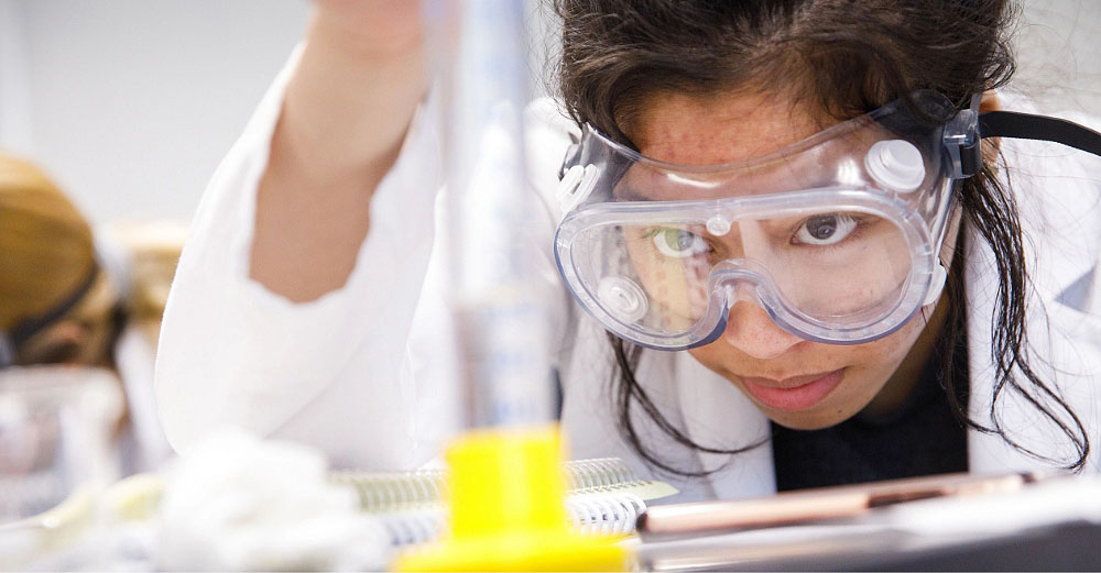 ASU student wearing a lab coat and goggles is focused on her work