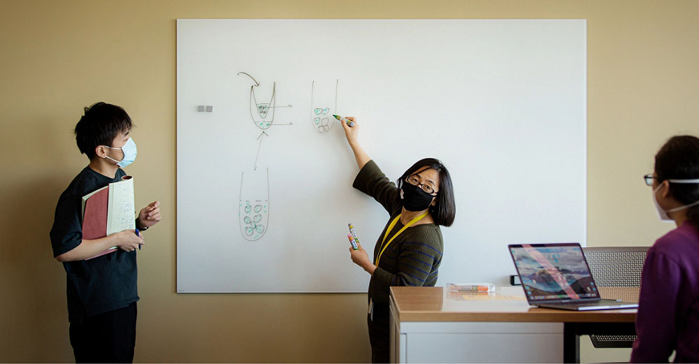 Three people discussing information written on a whiteboard