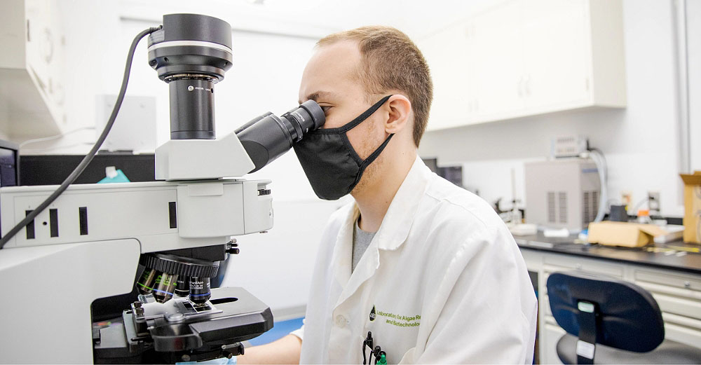 Male student is sitting at a desk and looking at something under a microscope