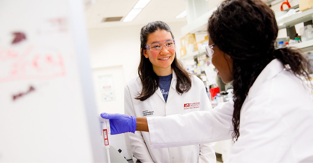 Two female students wearing lab coats having a conversation and smiling