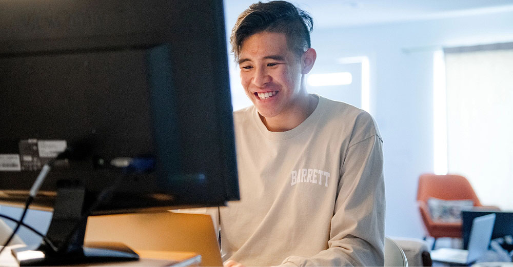 Enthusiastic male student types on desktop computer