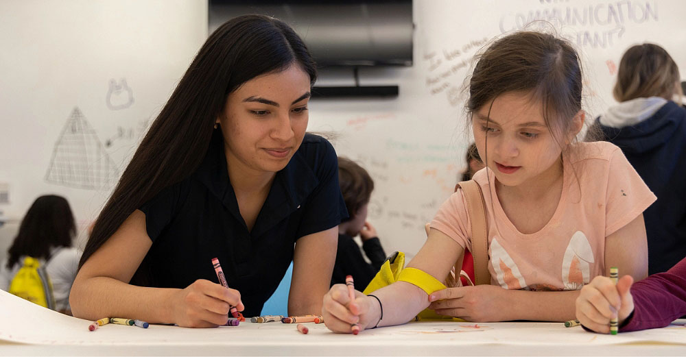 Young woman working with a little girl on coloring a page