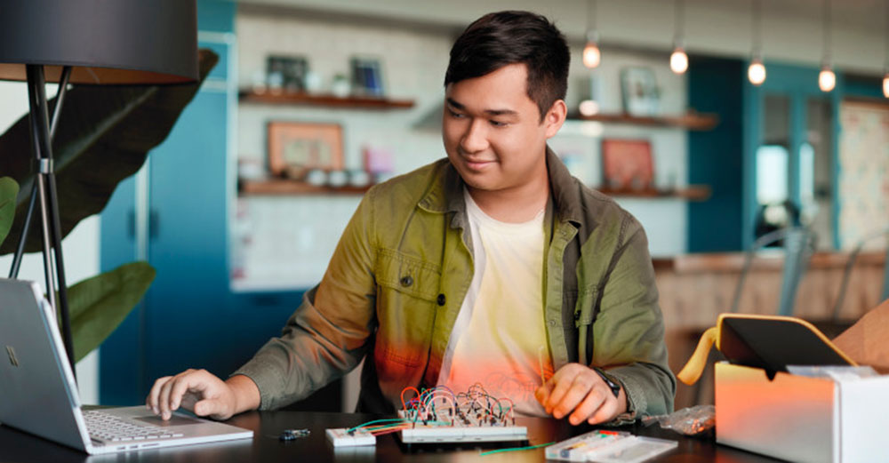 Male student working on a laptop and a take home lab kit