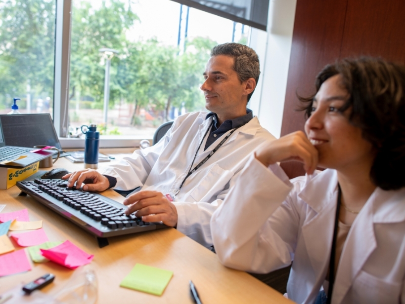 Male professor and female student look at a computer while smiling